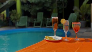 Una mesa con tres vasos de bebidas, un plato con rodajas de naranja y una piscina al fondo.