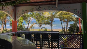 Un área de estar al aire libre con vista a la playa y al océano, que presenta un mural con notas musicales y vasos de cócteles.