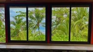 Una habitación con un ventanal grande que da a un paisaje tropical con palmeras y vistas al mar.