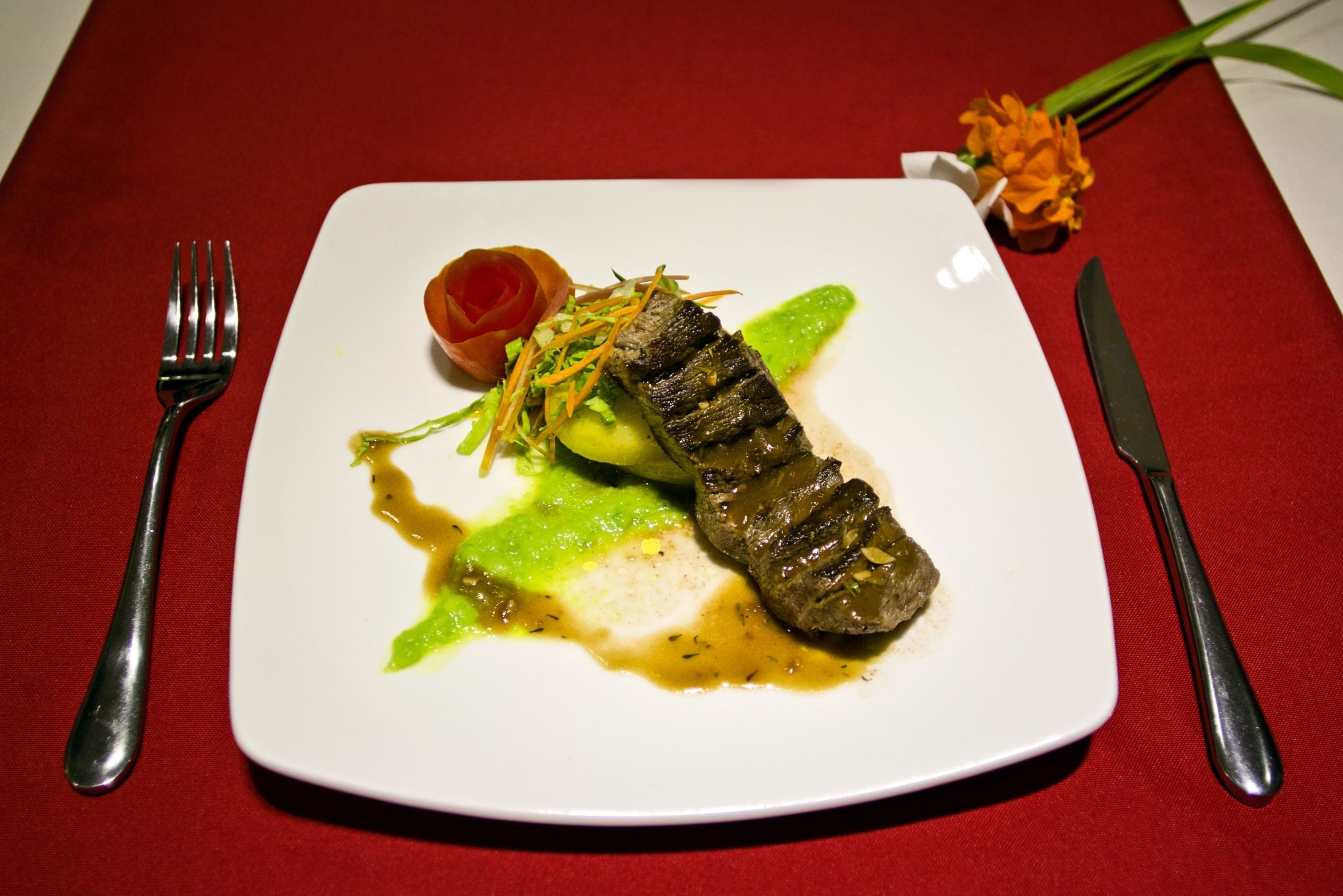 Un piatto bianco con una bistecca, salsa verde e una piccola salsa rossa su una tovaglia rossa.