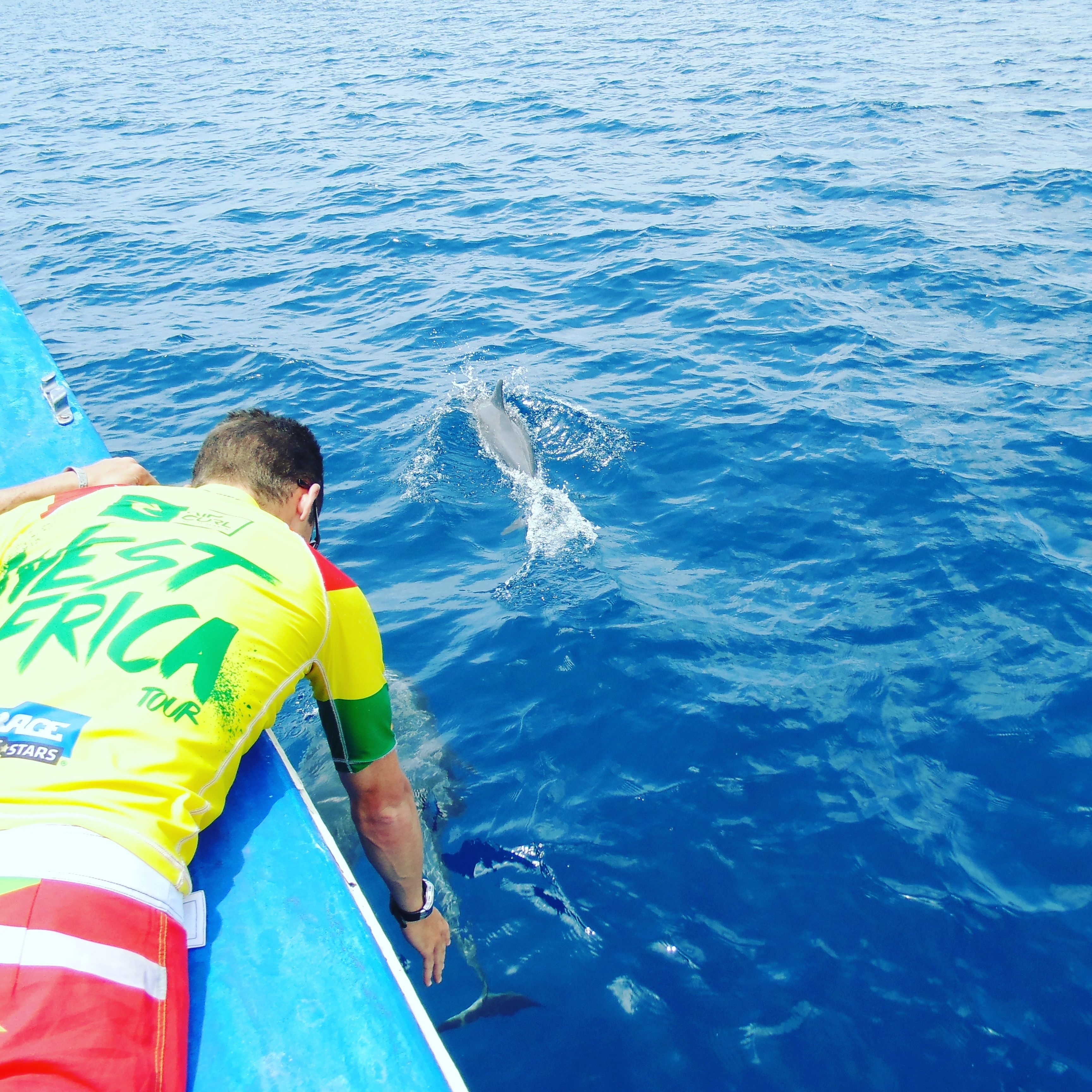 A person on a boat wearing a yellow and green shirt with text, looking at the ocean.