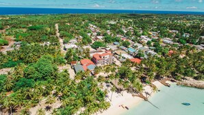 An aerial view of a coastal town with dense vegetation, a beach, and a mix of residential and commercial buildings.