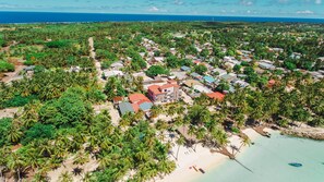 An aerial view of a coastal town with dense vegetation, a beach, and a mix of residential and commercial buildings.