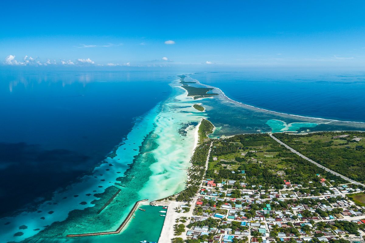 Vista aérea de un pueblo costero con mar azul cristalino, una playa de arena y un denso conjunto de edificios.