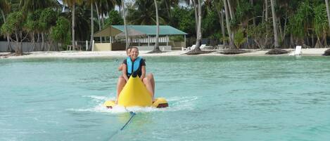 Une personne conduisant un véhicule nautique jaune sur une eau turquoise et limpide, entourée de palmiers et d’une plage avec des chaises longues.