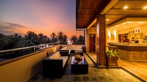 A rooftop terrace with seating, a bar area, and a view of palm trees at sunset.