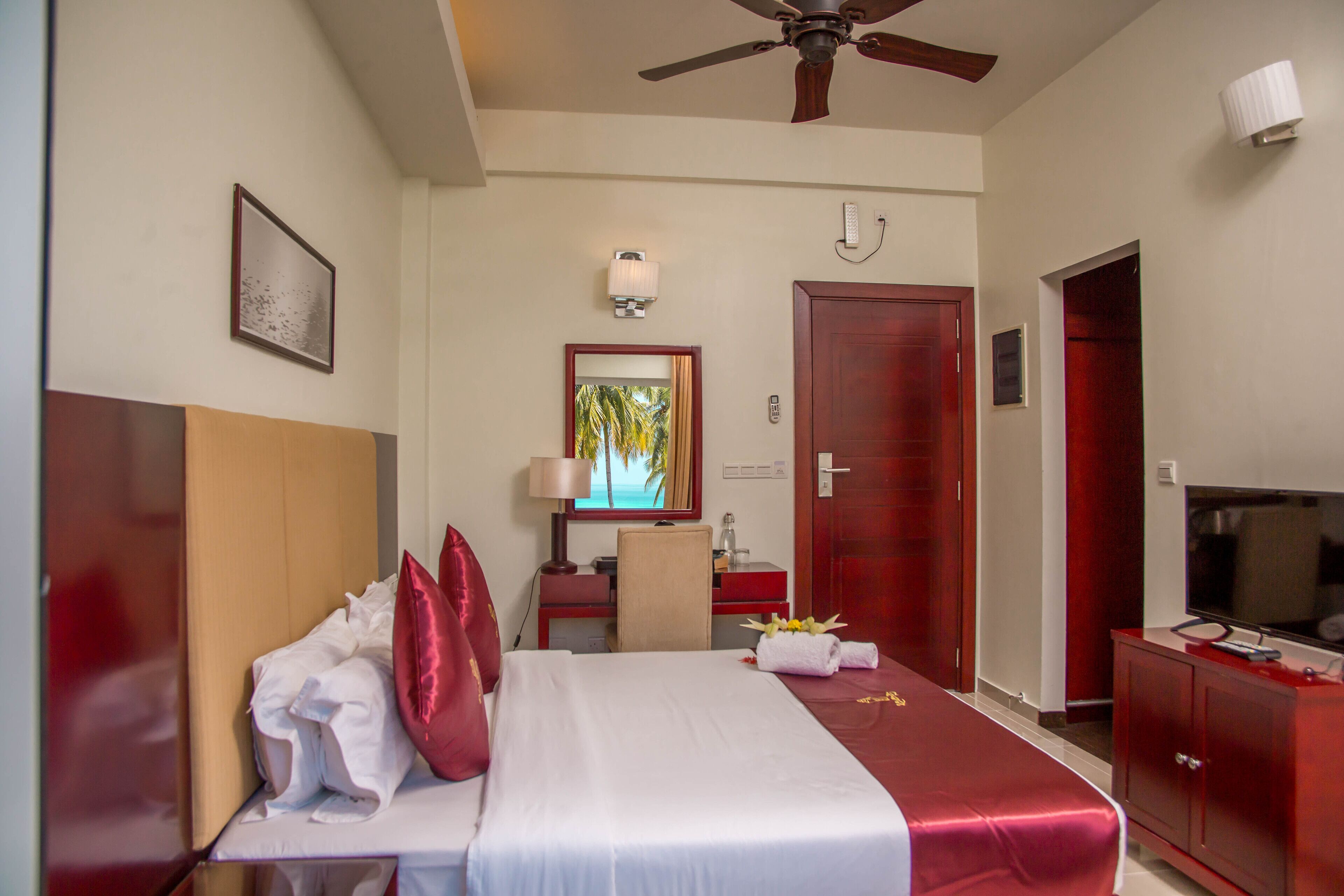 Una habitación de hotel con cama, escritorio, televisión y ventilador de techo.