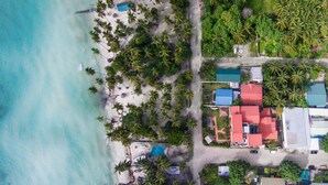 Vista aérea de una zona costera con playa, palmeras y edificios con techos rojos.