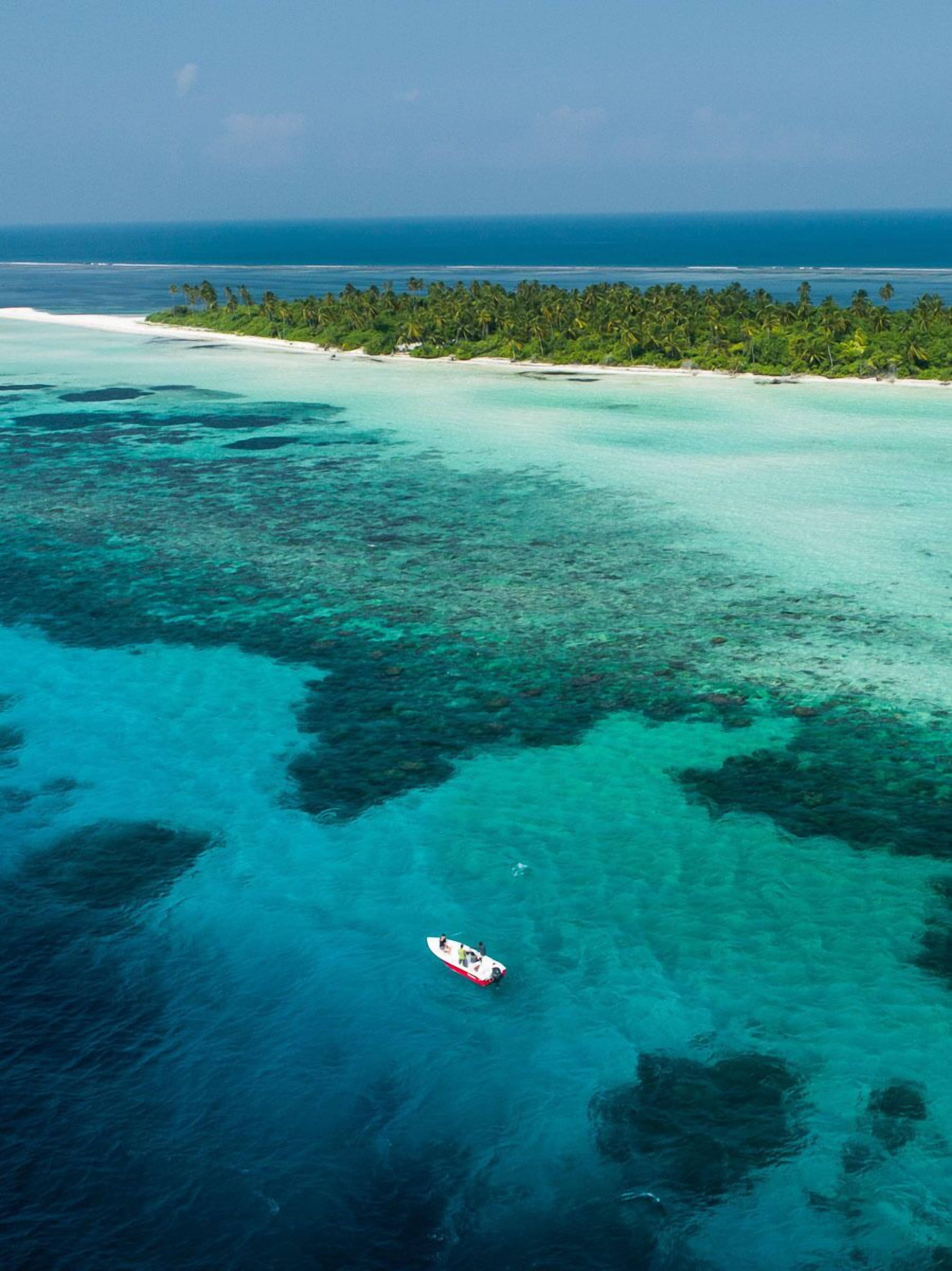 An aerial view of a tropical island with clear turquoise waters, a small boat, and a dense forested area.