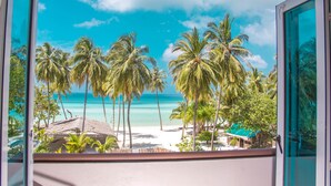 Vista desde un balcón sobre una playa con palmeras y un cielo azul despejado.