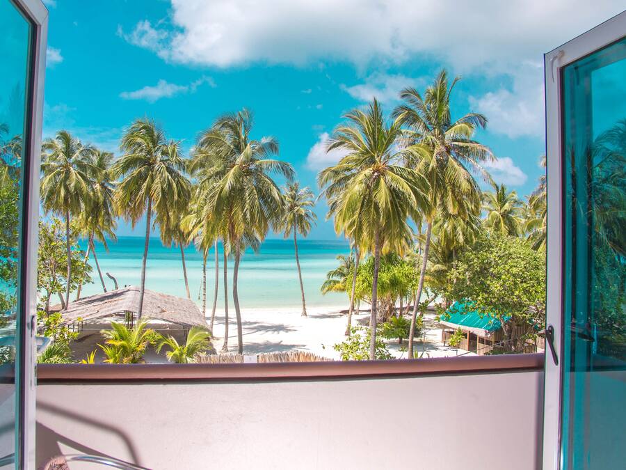 Blick vom Balkon auf einen Strand mit Palmen und blauem Himmel.