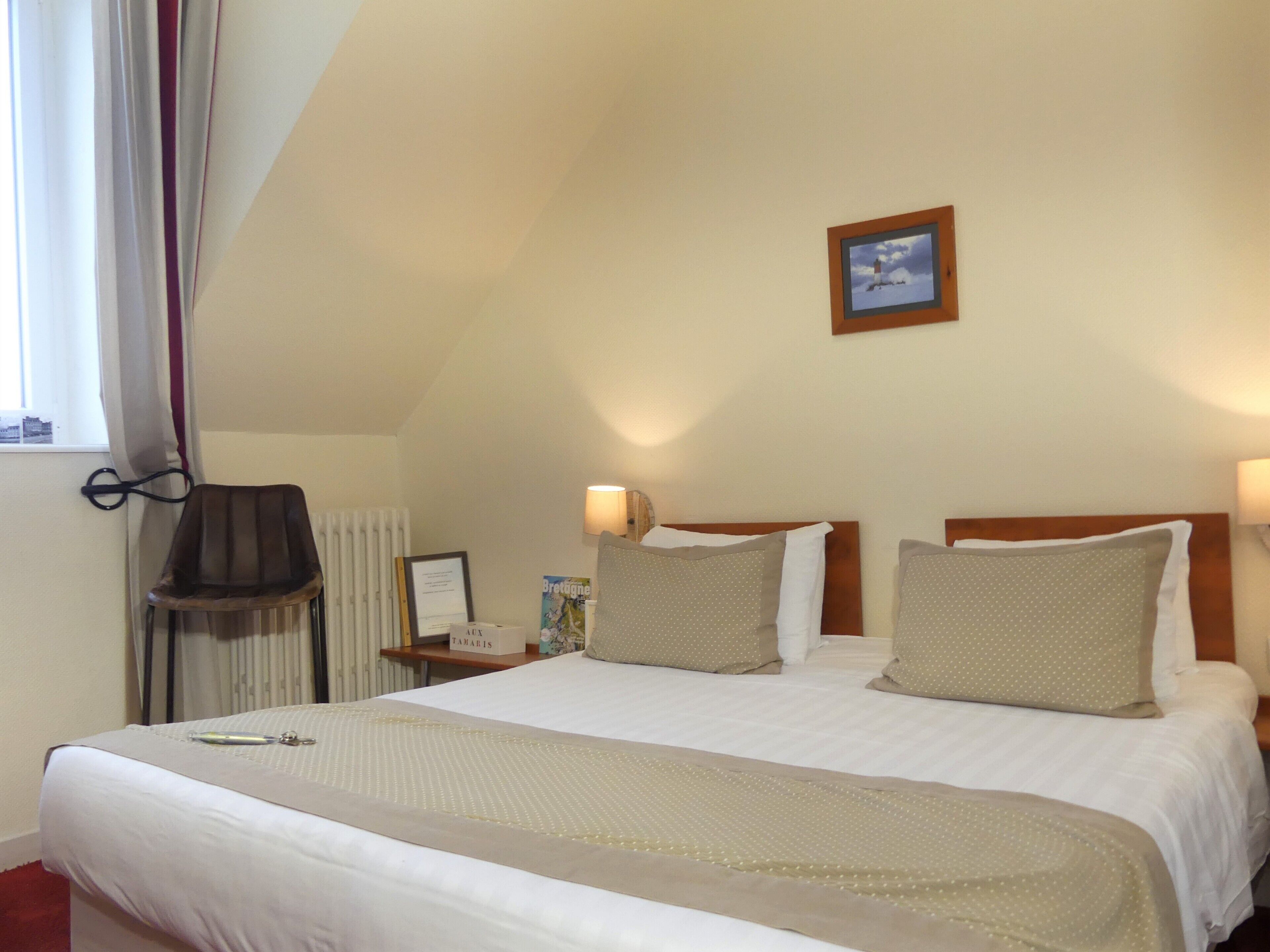 A hotel room with a large bed, two bedside tables, a chair, a radiator, a framed certificate, and a picture on the wall.