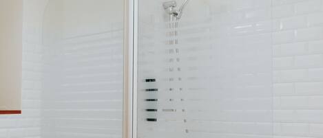 Un baño con lavamanos blanco, espejo y ducha con mampara de vidrio.