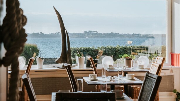 A dining area with a view of the sea, featuring a table set with plates, glasses, and cutlery. - Hôtel Aux Tamaris - Vue Mer (Roscoff)