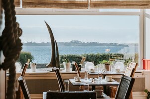 Un coin repas avec vue sur la mer, où une table est dressée avec des assiettes, des verres et des couverts.