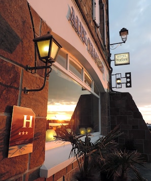 A hotel entrance with a sign reading "HOTEL AUX TAMARIS" and a "H" sign indicating a hotel.