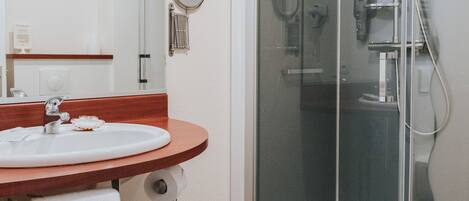 Un baño con piso de madera, un lavamanos blanco con espejo y una ducha con mampara de vidrio.