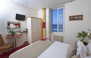 A hotel room with a bed, a desk with a chair, a television, a window with a view of the sea, and a framed picture on the wall. - Hôtel Aux Tamaris - Vue Mer (Roscoff)