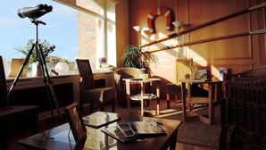 A sunlit room with wicker furniture, a telescope, and a life ring on the wall. - Hôtel Aux Tamaris - Vue Mer (Roscoff)