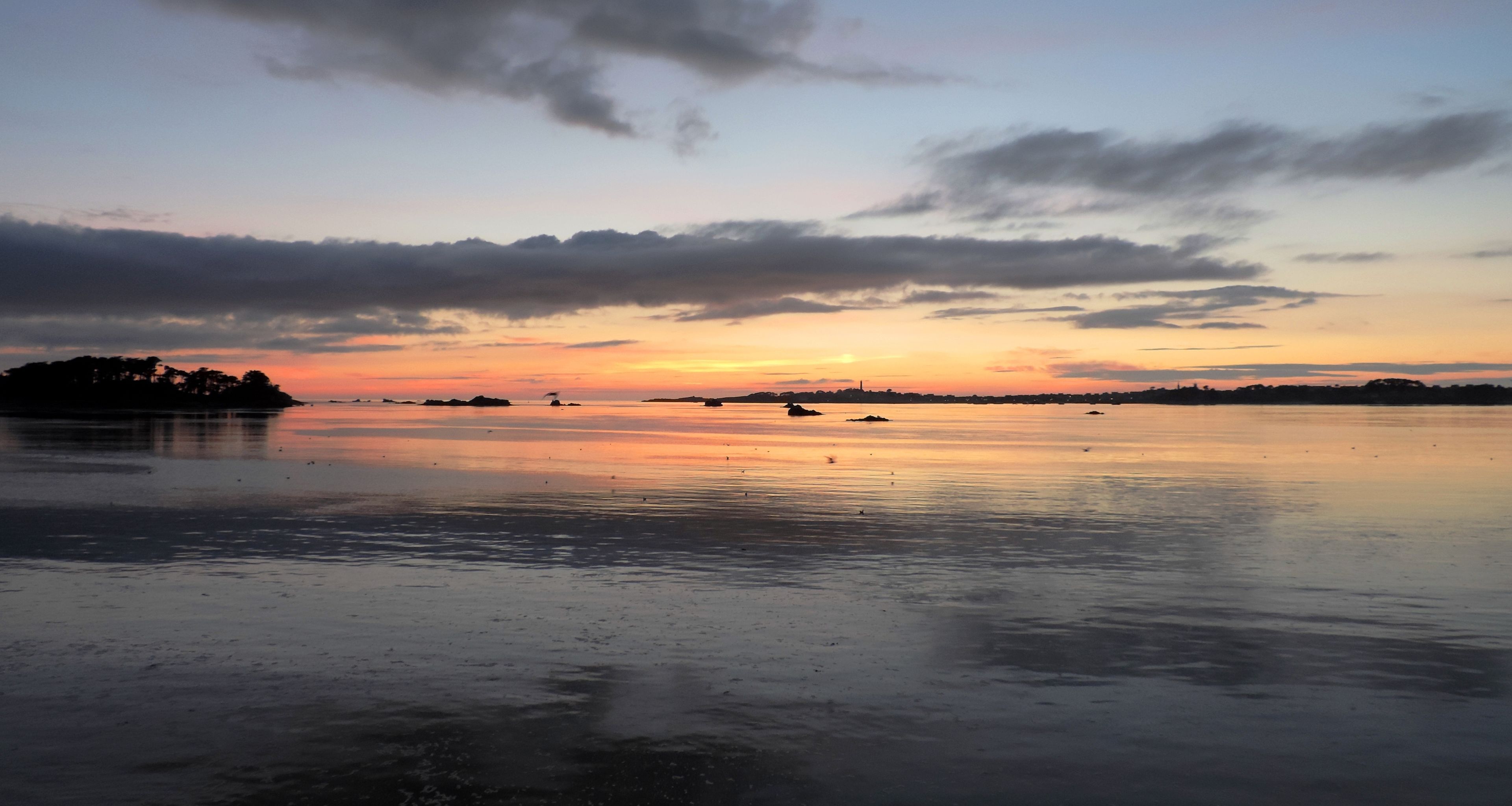 A calm body of water reflecting the sky during sunset with distant land silhouettes.