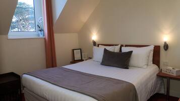 A neatly made bed with a brown blanket, a nightstand with a lamp, and a window with curtains.