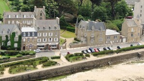 A model of a historic building with multiple windows and a central entrance, surrounded by a landscaped garden and a parking area with several cars. - Hôtel Aux Tamaris - Vue Mer (Roscoff)
