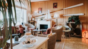 A cozy living room with wicker furniture, a fireplace, and a large window. - Hôtel Aux Tamaris - Vue Mer (Roscoff)