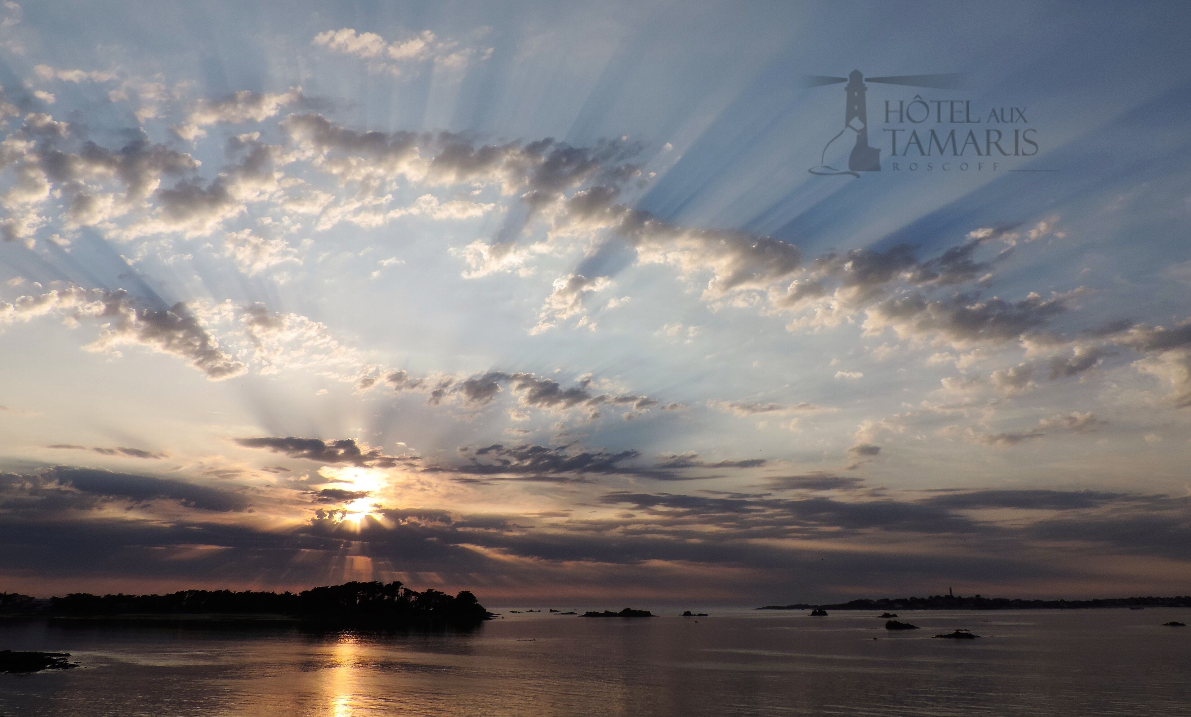 Un coucher de soleil sur une étendue d’eau, avec des nuages, et le logo de l’« Hôtel aux Tamaris Roscoff » dans le coin supérieur droit.
