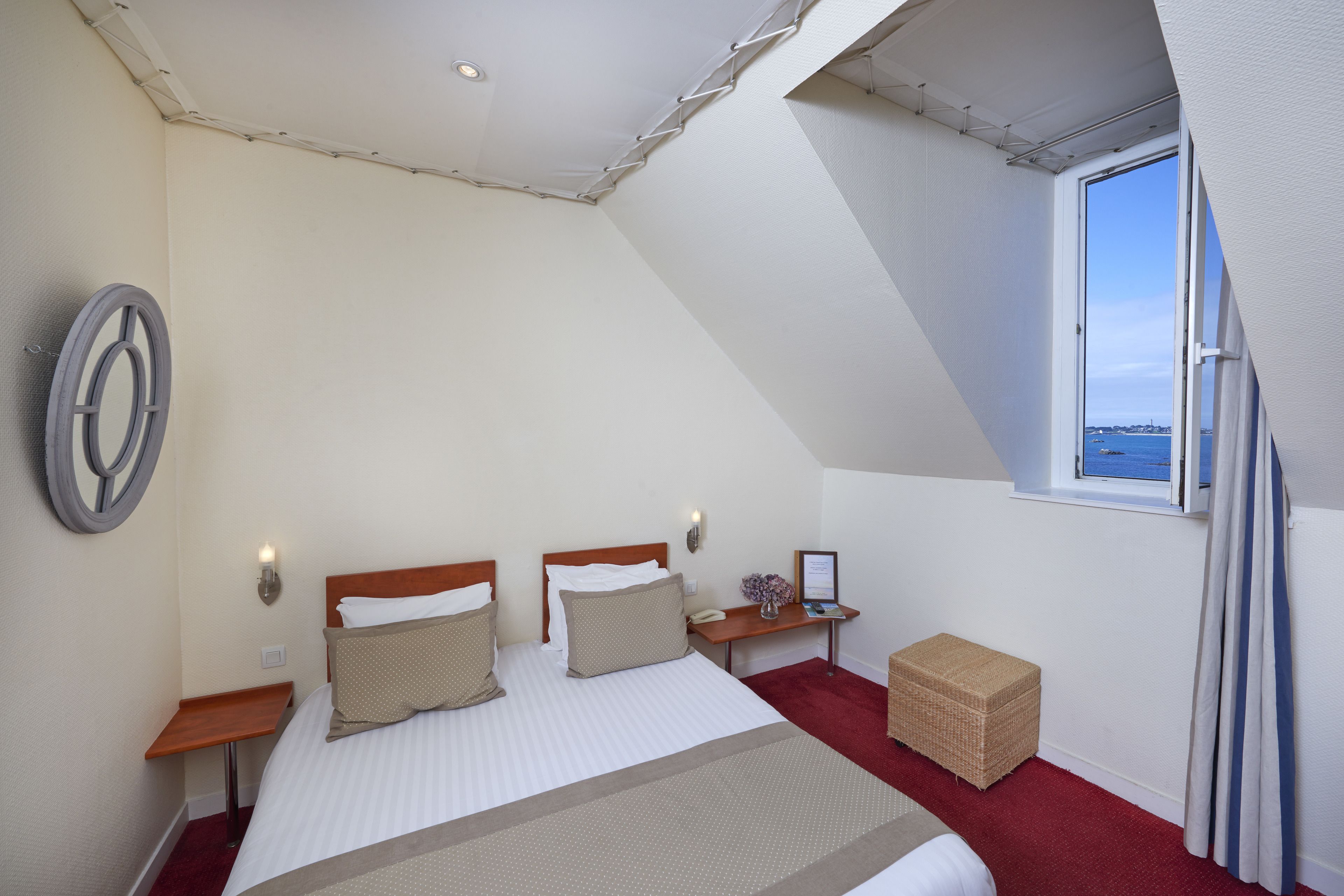 Una camera da letto con un letto, due comodini, un tavolino da notte, una finestra con tende e vista sul mare.