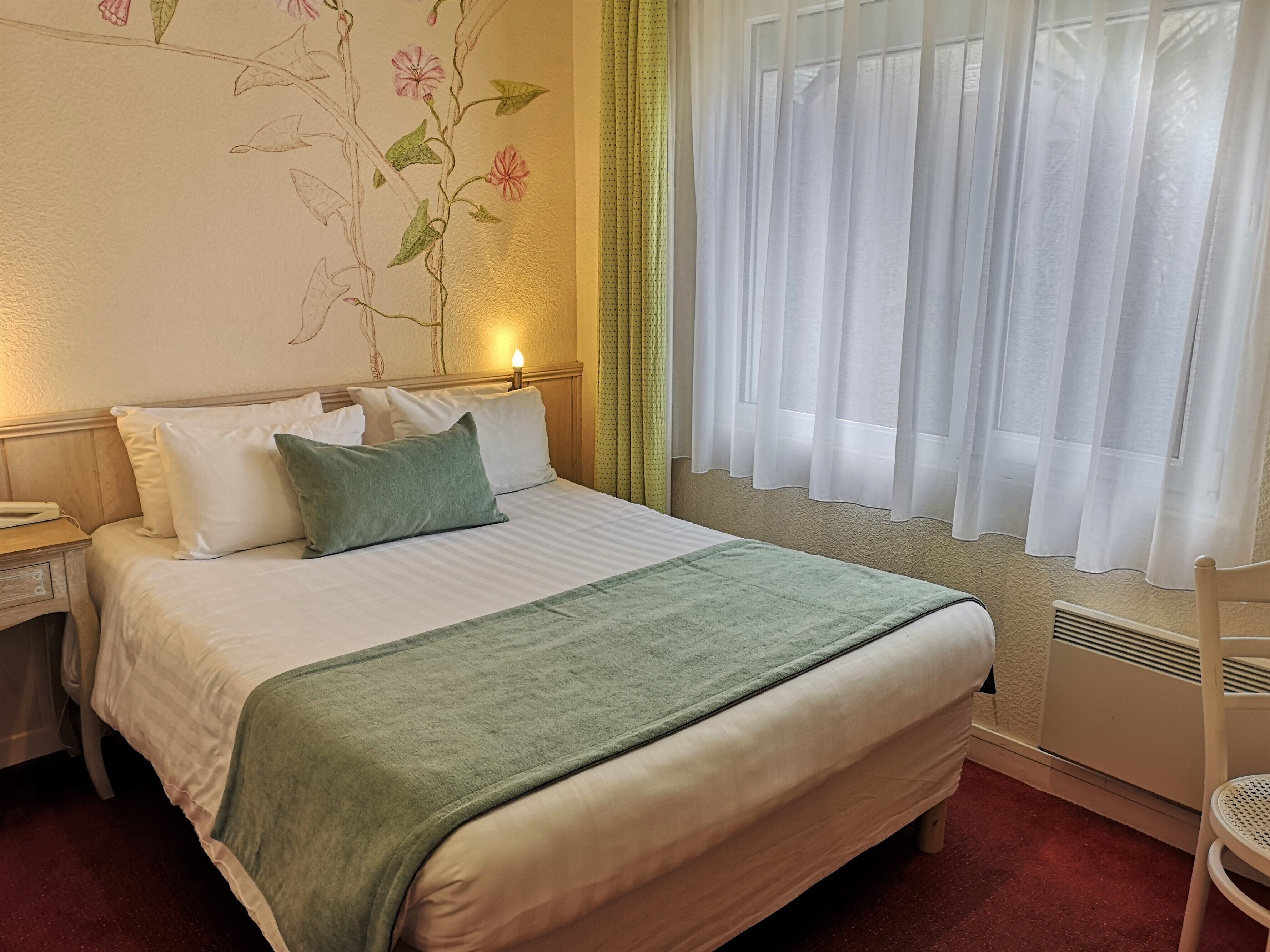 Una cama bien hecha con un plaid verde, almohadas blancas y un mural floral.