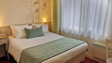 Una cama bien hecha con un plaid verde, almohadas blancas y un mural floral.