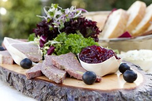 A wooden board with sliced meats, a bowl of red berries, and some bread. - Hotel Restaurant Vijlerhof (Vijlen)