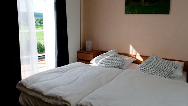 A hotel room with a large bed, a nightstand, a lamp, and a painting of a castle on the wall. - Hotel Restaurant Vijlerhof (Vijlen)