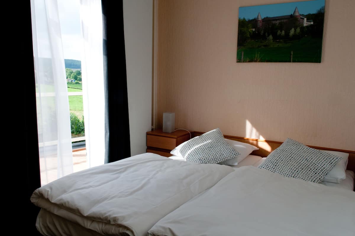 Ein Hotelzimmer mit einem großen Bett, einem Nachttisch, einer Lampe und einem Schlossgemälde an der Wand.