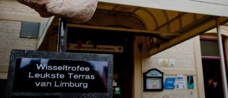 Un gesto de pulgar hacia arriba con el texto 'Vijlerhof' y una placa que dice 'Premio al mejor patio de Limburgo 2012'.