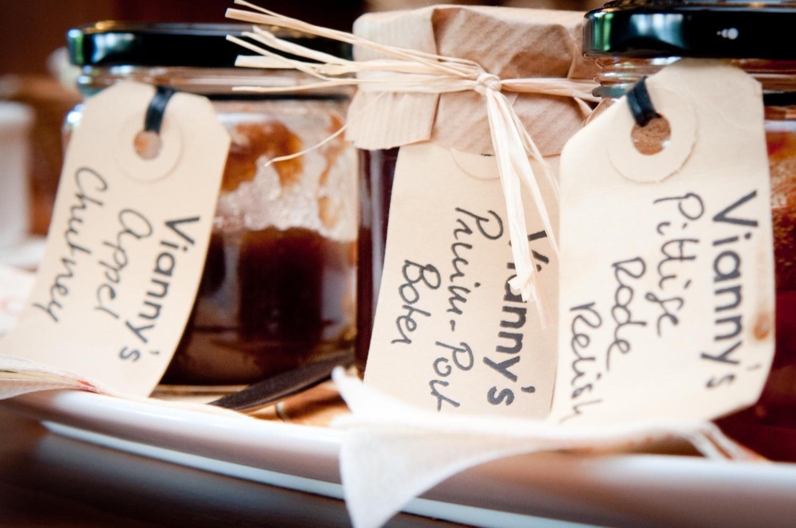 Three glass jars with labels, tied with twine, containing different types of preserves.