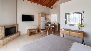 A bedroom with a bed, a TV, a wooden ceiling, a kitchen area, and a desk with a vase. - Anassia Villas (Nafplio)
