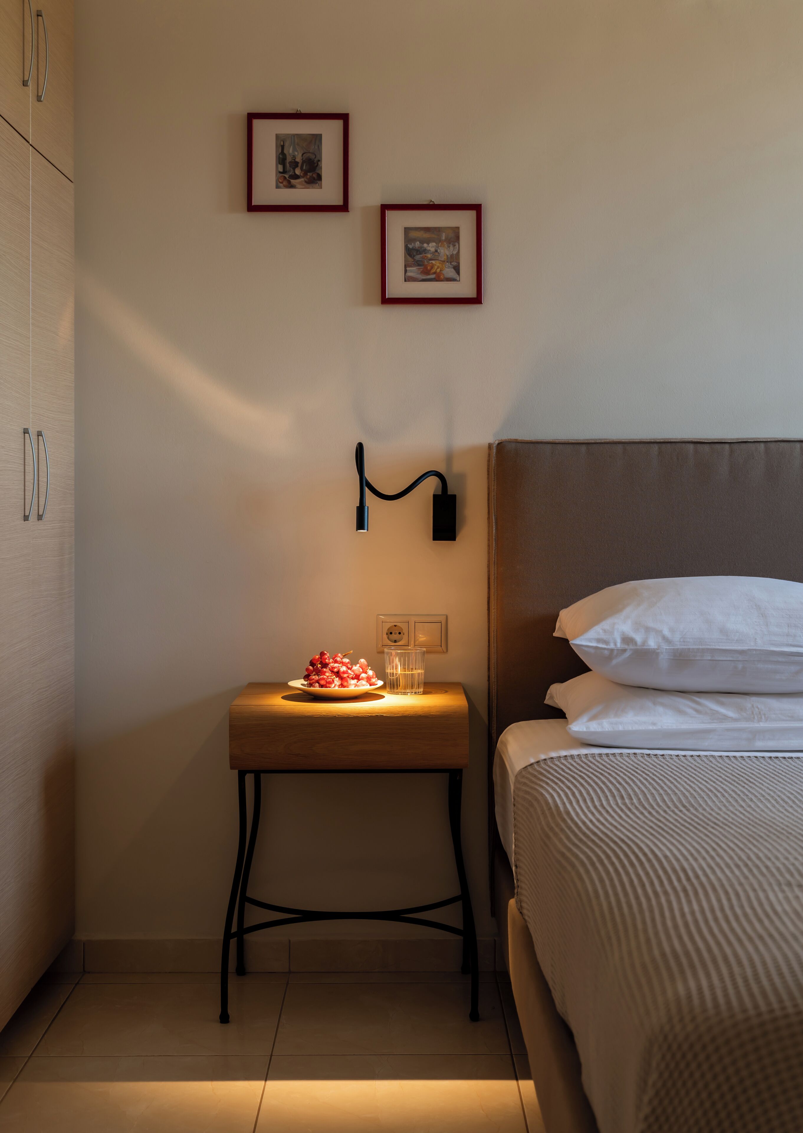 Une chambre à coucher avec un lit, une table de chevet avec une lampe, et deux tableaux encadrés accrochés au mur.