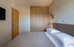 Un dormitorio con cama, armario, mesita de noche y televisor montado en la pared.
