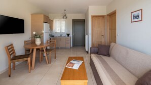 A modern living room with a sofa, coffee table, dining table, and chairs. - Anassia Villas (Nafplio)