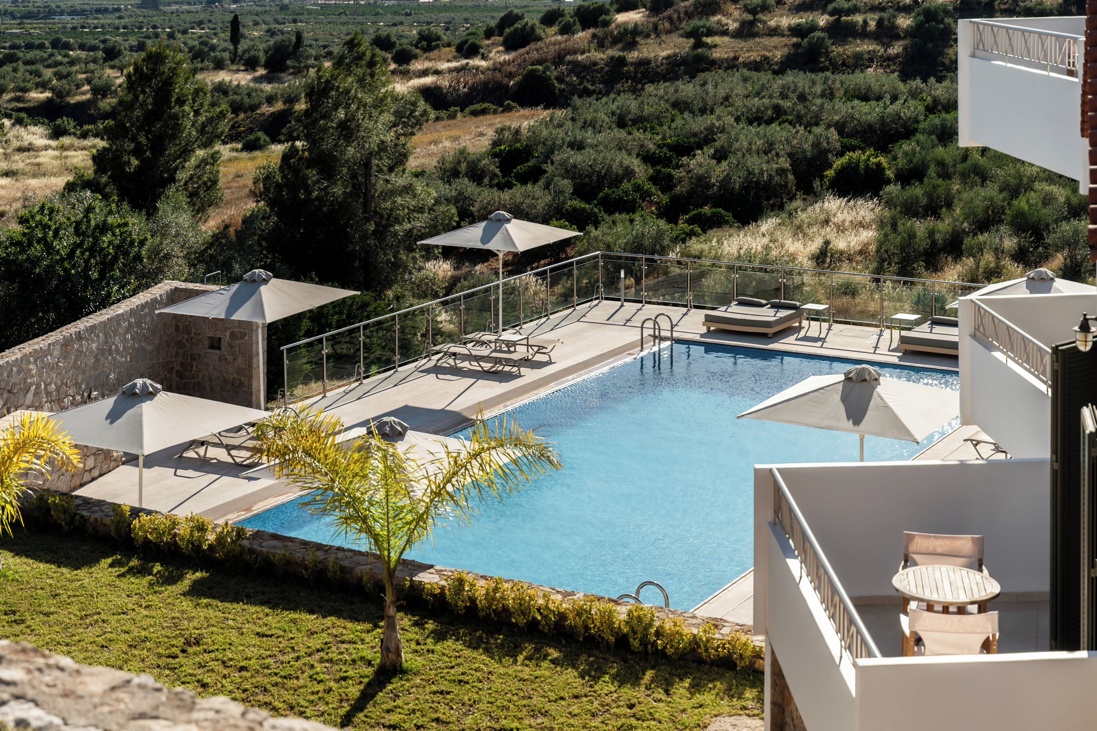 Una piscina con sillas de descanso y sombrillas, rodeada de vegetación y un muro de piedra.