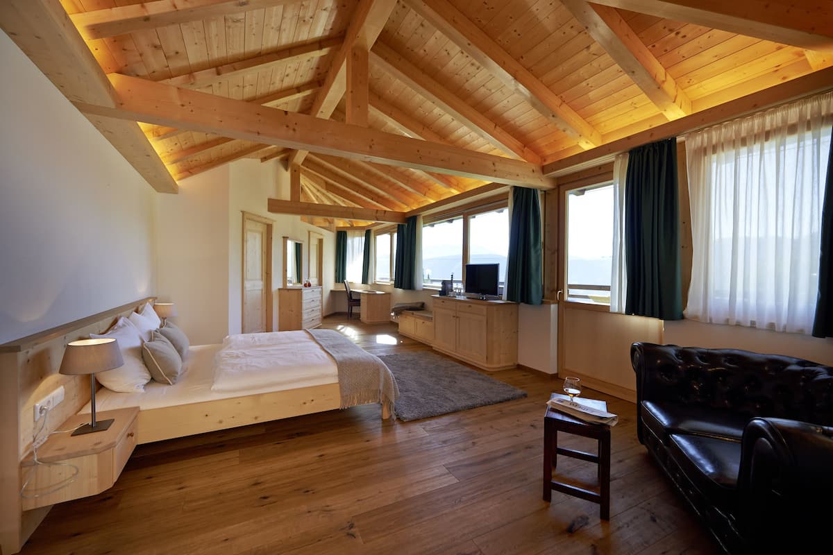 Ein geräumiges Zimmer mit Holzbalkendecke, einem Bett, einer Couch und einem Schreibtisch.