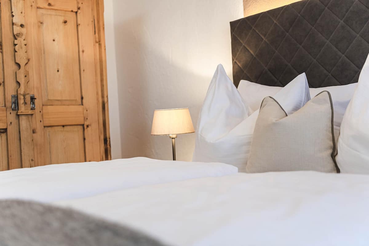 Ein ordentlich bezogenes Bett mit weißen Leinen und mehreren Kissen, eine Holztür und ein moderner Bettrahmen.