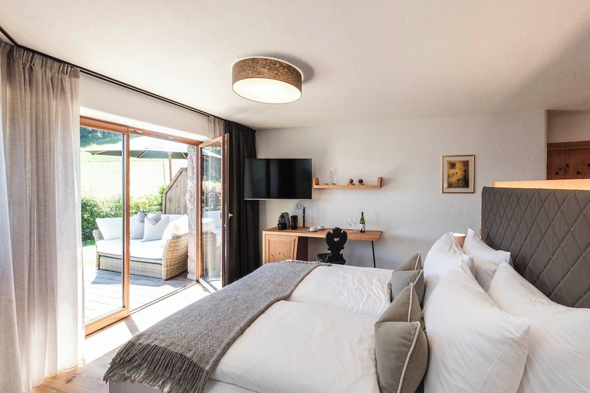 Ein Schlafzimmer mit Bett, Schreibtisch, Fernseher und Blick ins Freie.