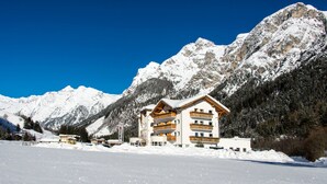 Un edificio de varios pisos con balcones, rodeado de montañas nevadas y un cielo azul despejado.