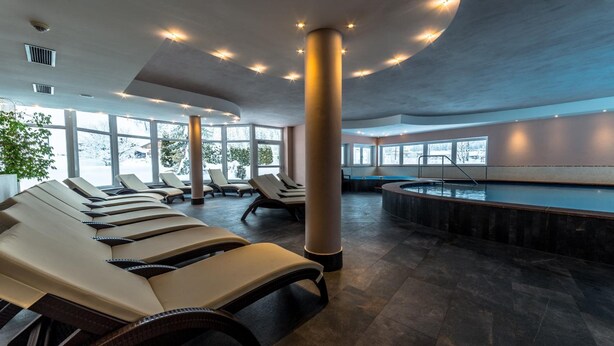 Zona de spa con tumbonas, piscina y ventanas amplias.