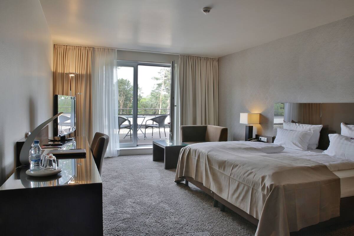 Une chambre d’hôtel équipée d’un lit, d’un bureau, d’une chaise, d’une lampe et offrant une vue sur l’extérieur.