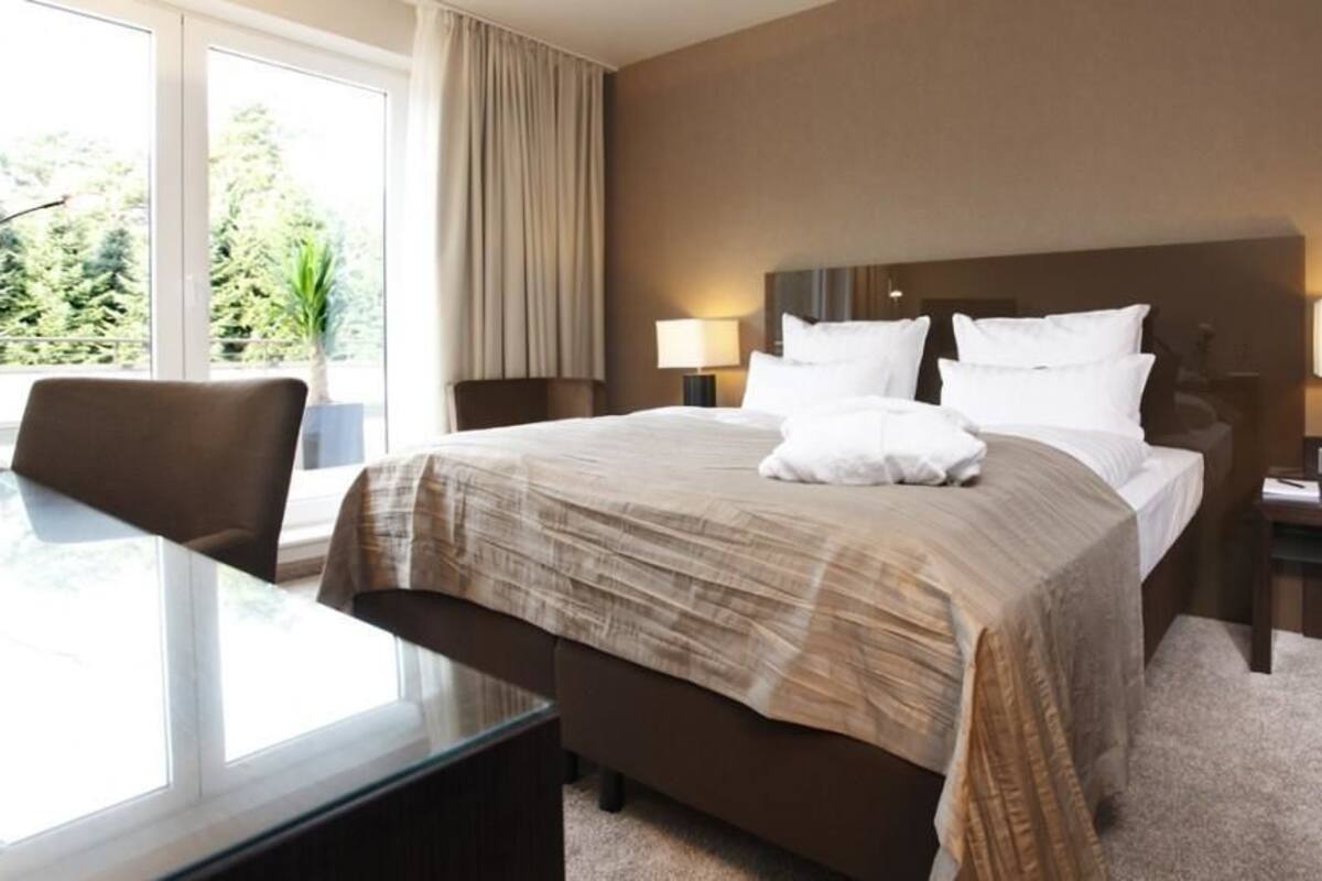 Une chambre d’hôtel avec un grand lit, deux tables de chevet avec des lampes, une chaise et une vue sur la verdure.