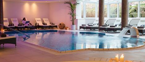 A modern indoor pool area with lounge chairs, a large plant, and candles.