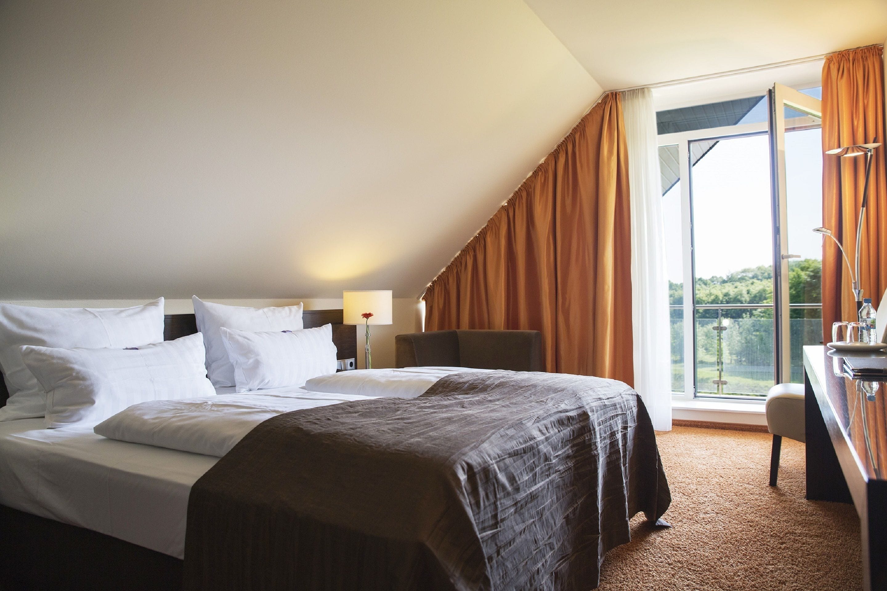Quarto de hotel com uma cama grande, uma mesa de trabalho com cadeira e varanda com cortinas.